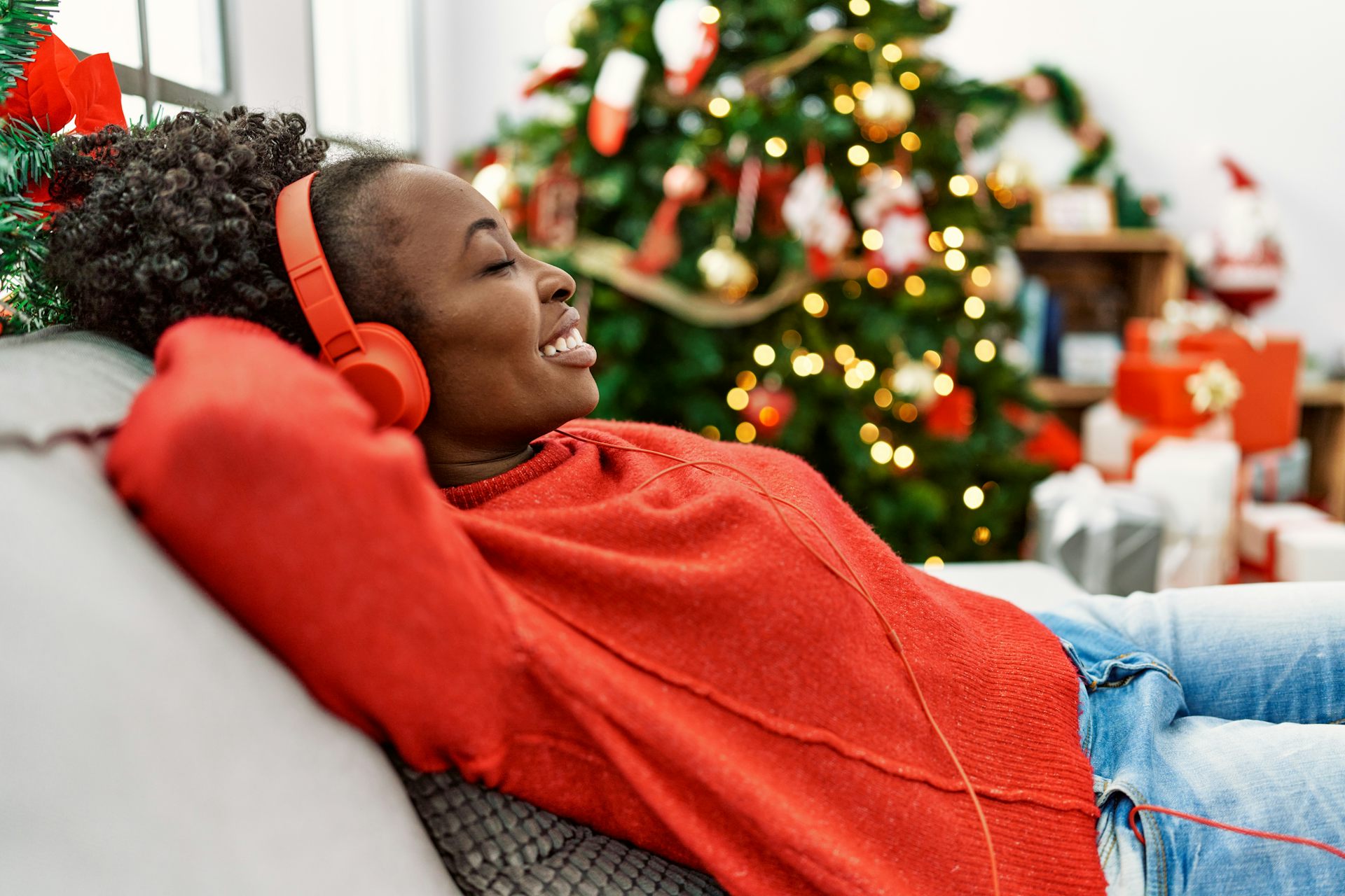 Woman listening to Christmas songs on her headphones with a tree in the background