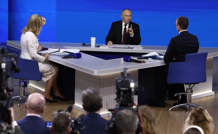 Vladimir Putin appears with two TV presenters at a press conference.