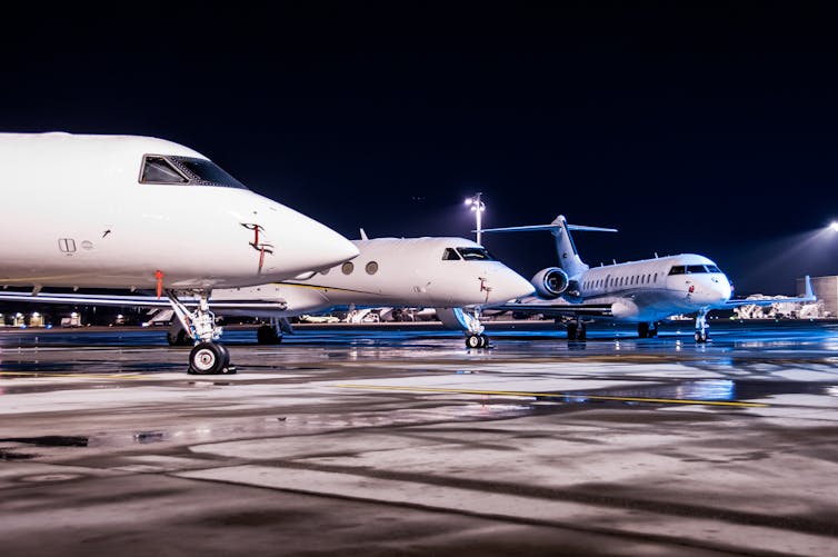 private jets lined up on the apron at an airport at night time.