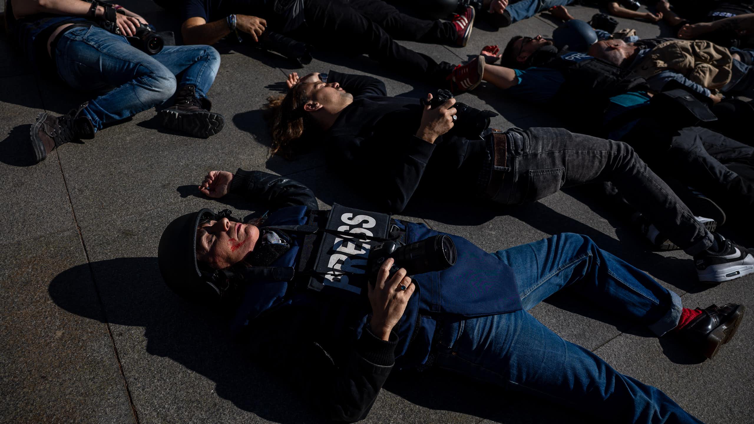 Photographers and journalists in 'press' jackets lying on the ground as if dead