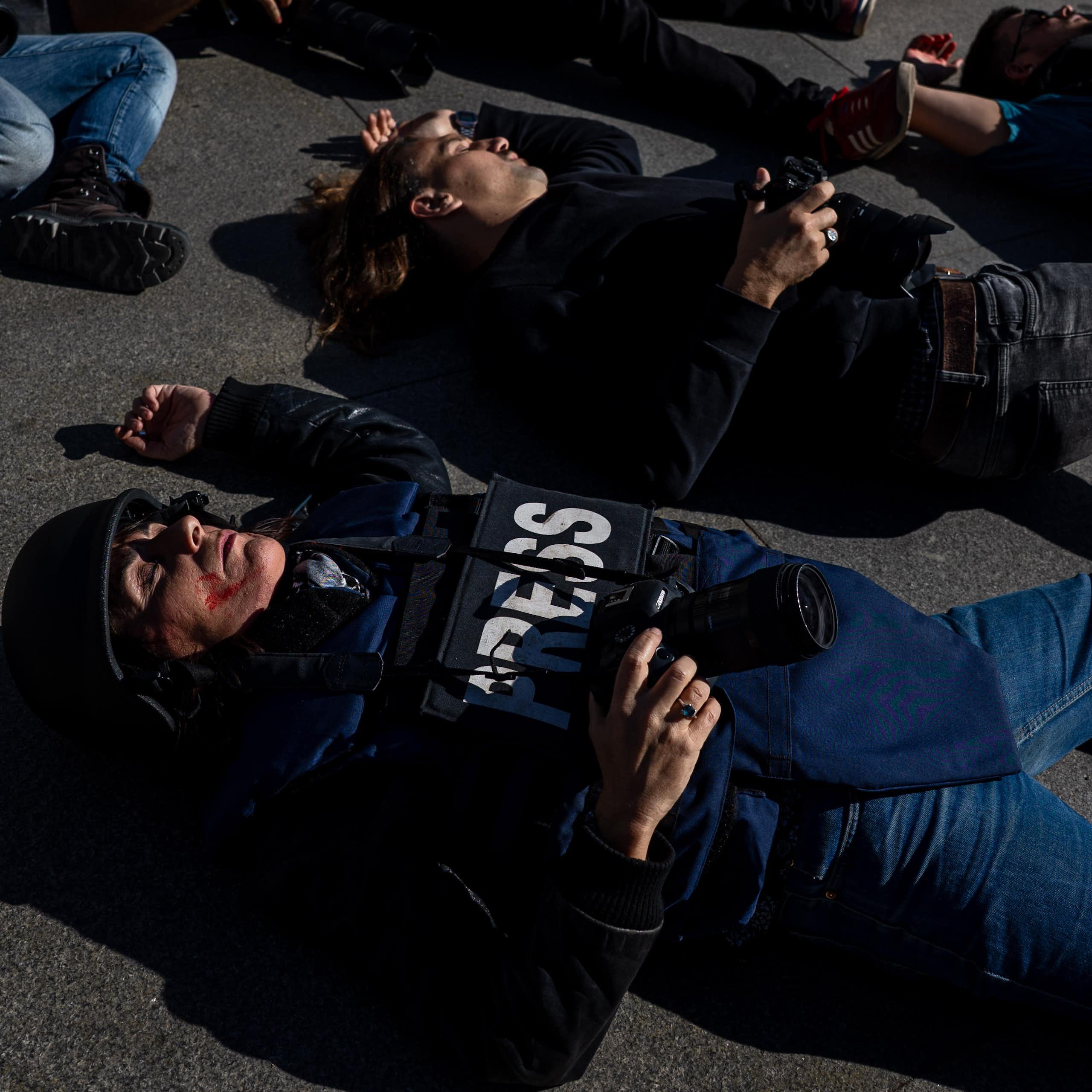 Photographers and journalists in 'press' jackets lying on the ground as if dead