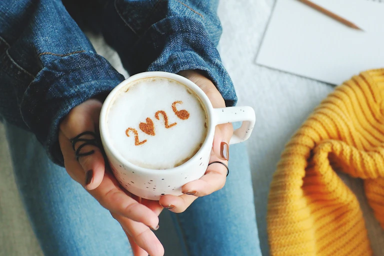 Close up of woman's hands holding a latte with 2026 written in cinnamon.