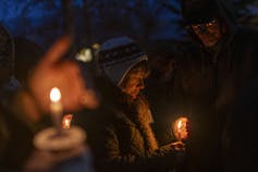 People stand in the dark holding lit candles.