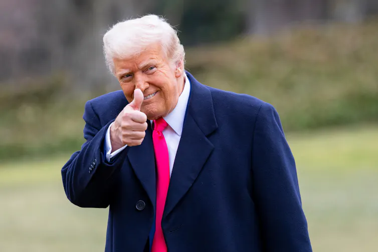 Strange-looking orange-faced old man with thumbs up and a red tie that goes down to his knees.