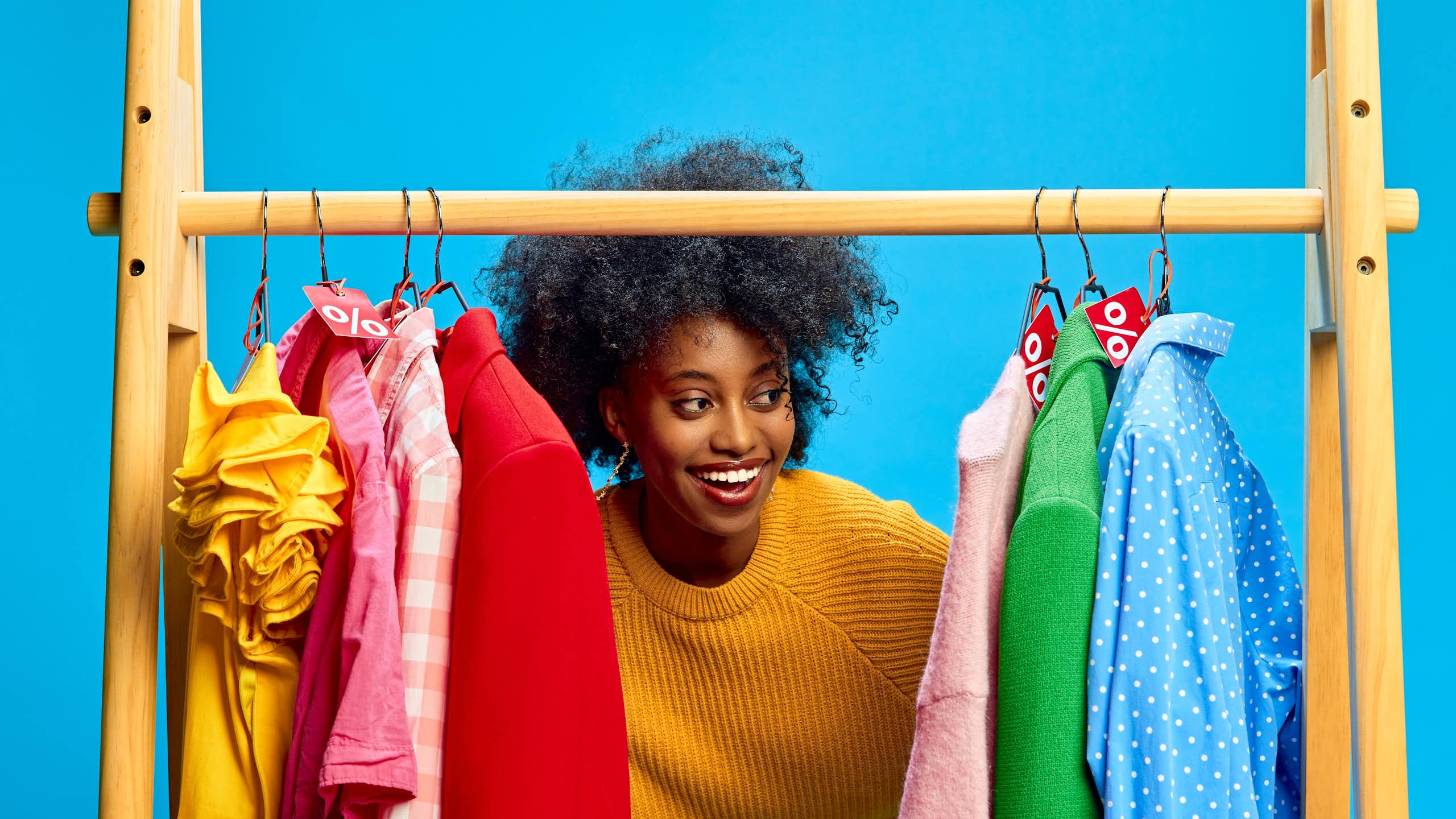 woman looks at colourful rail of clohtes, blue background