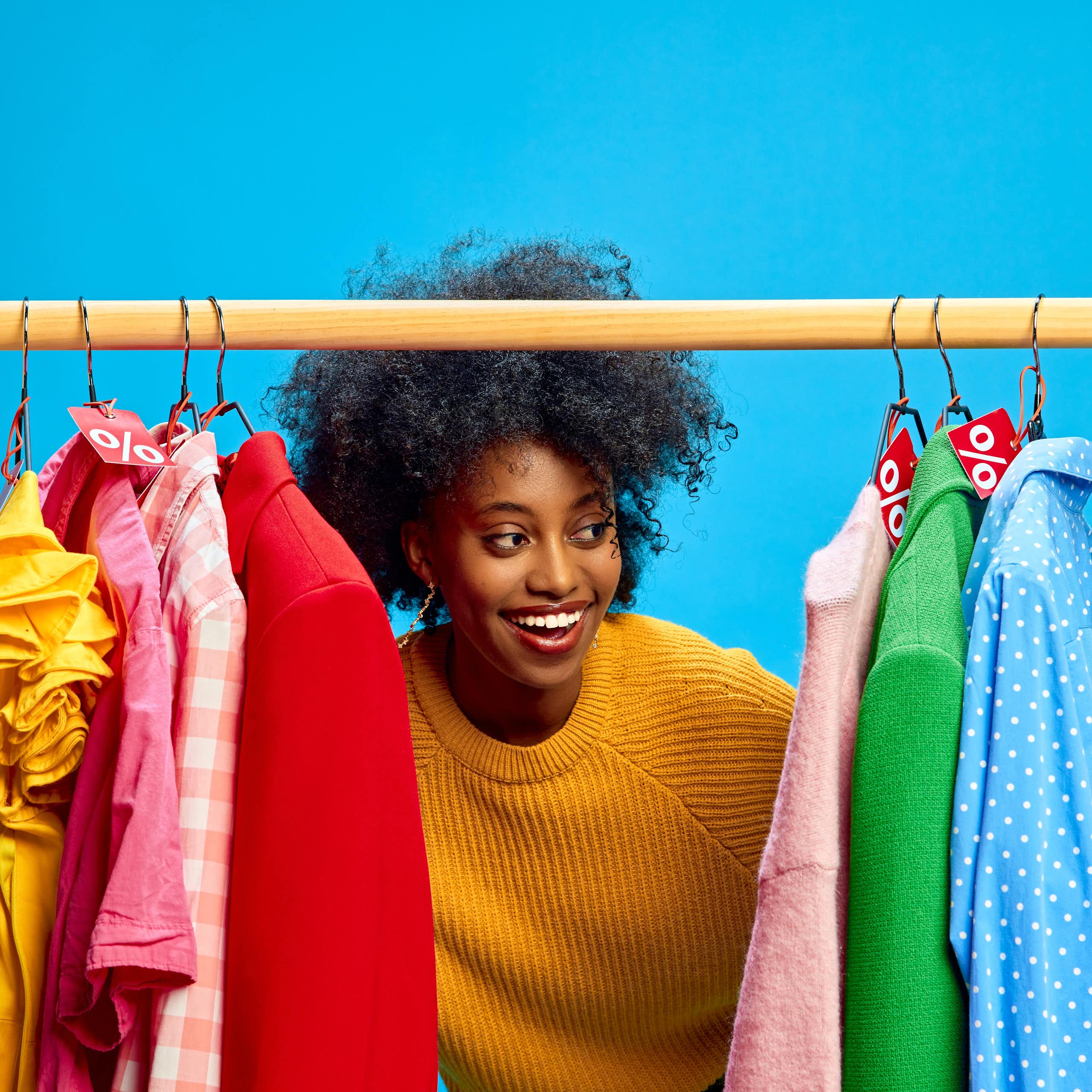 woman looks at colourful rail of clohtes, blue background