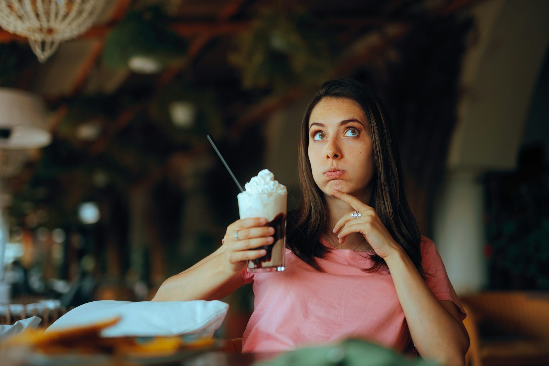 Woman sits in cafe holding a drink with a lot of whipped cream