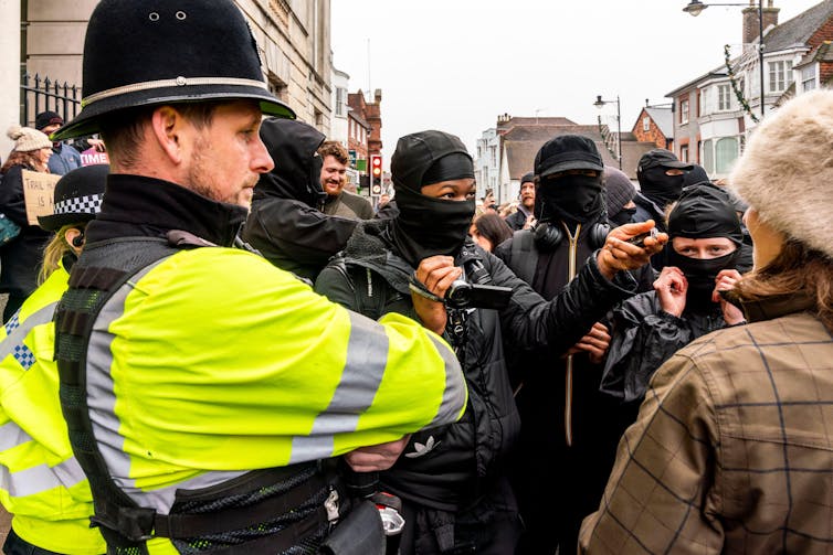 Meet these days’s hunt saboteurs – ‘doctors, teachers, even farmers’ operating with police to deliver unlawful fox hunts to justice 5 Pro- and anti-hunt groups confront each other in a street as a policeman watches on.