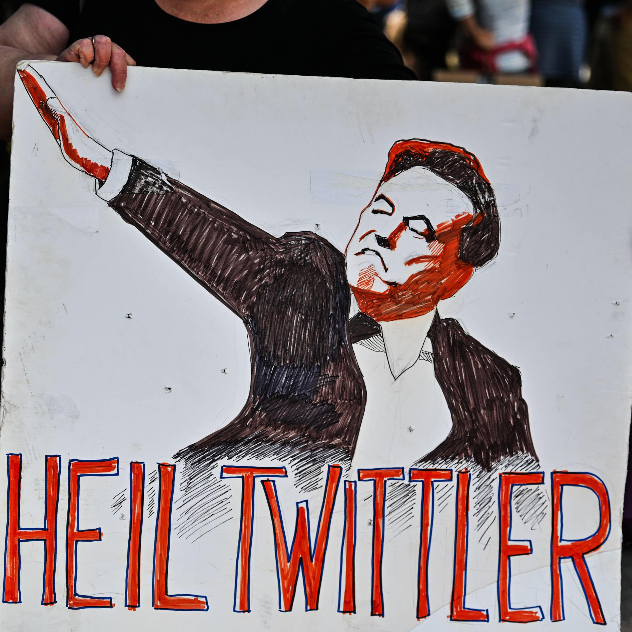 A protester holds up a sign featuring an illustration of Elon Musk and the words 'heil twittler'.