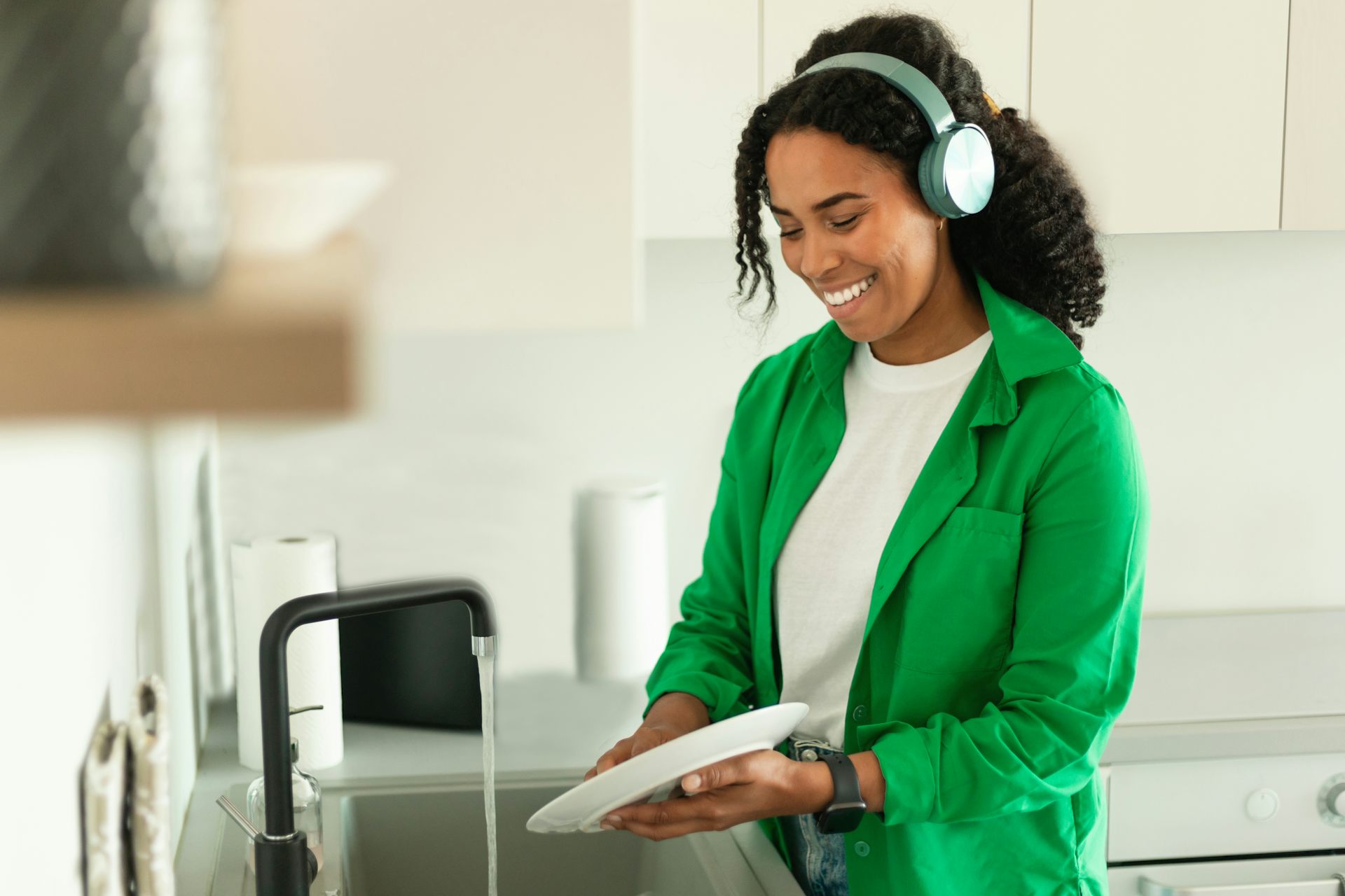 Woman with headphones smiling while she washes dishes
