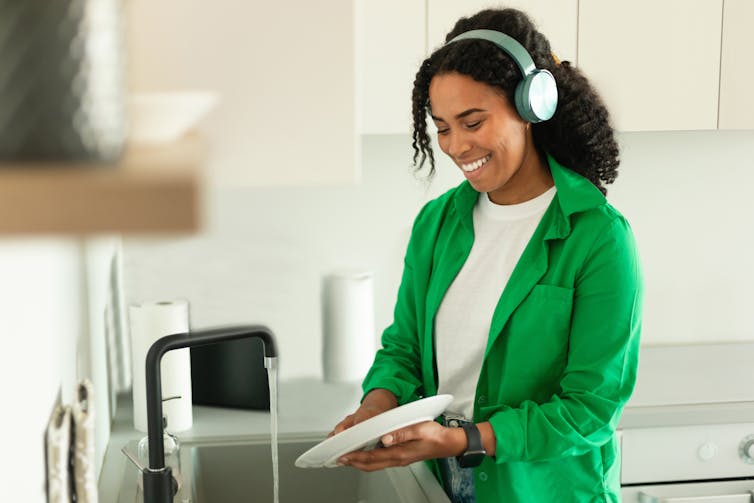 Woman with headphones smiling while she washes dishes