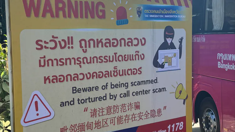 A large yellow roadside sign at a Thai immigration checkpoint warning travellers to be aware of scams and torture across the border.