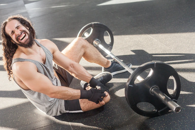 Man cries his pain after hurting knee while lifting weights