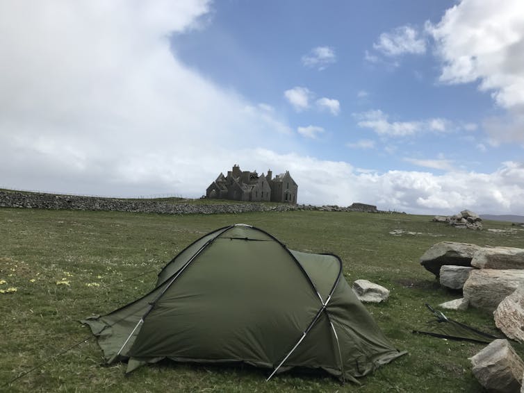 Green tent in front of derelict building.