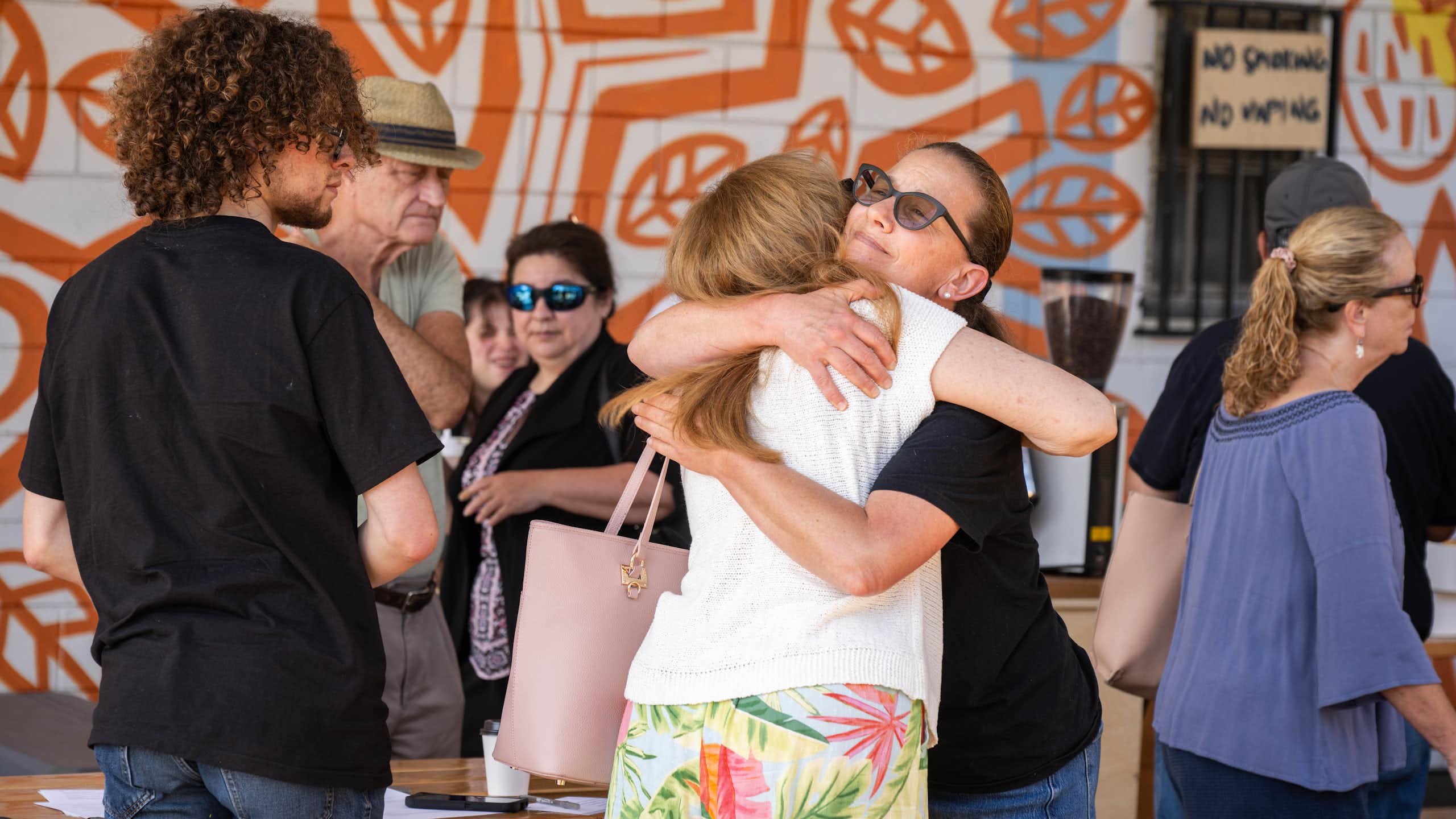 Two women hug with a group of neighbors from all ages around them.