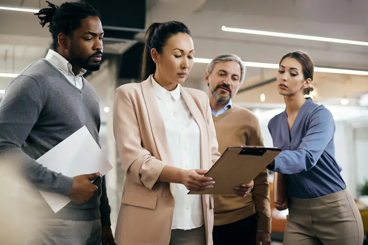 A group of people stand behind a woman who is holding a clipboard in front of her