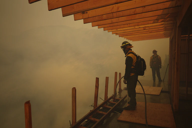 Firefighters stand on a deck as smoke rolls in.