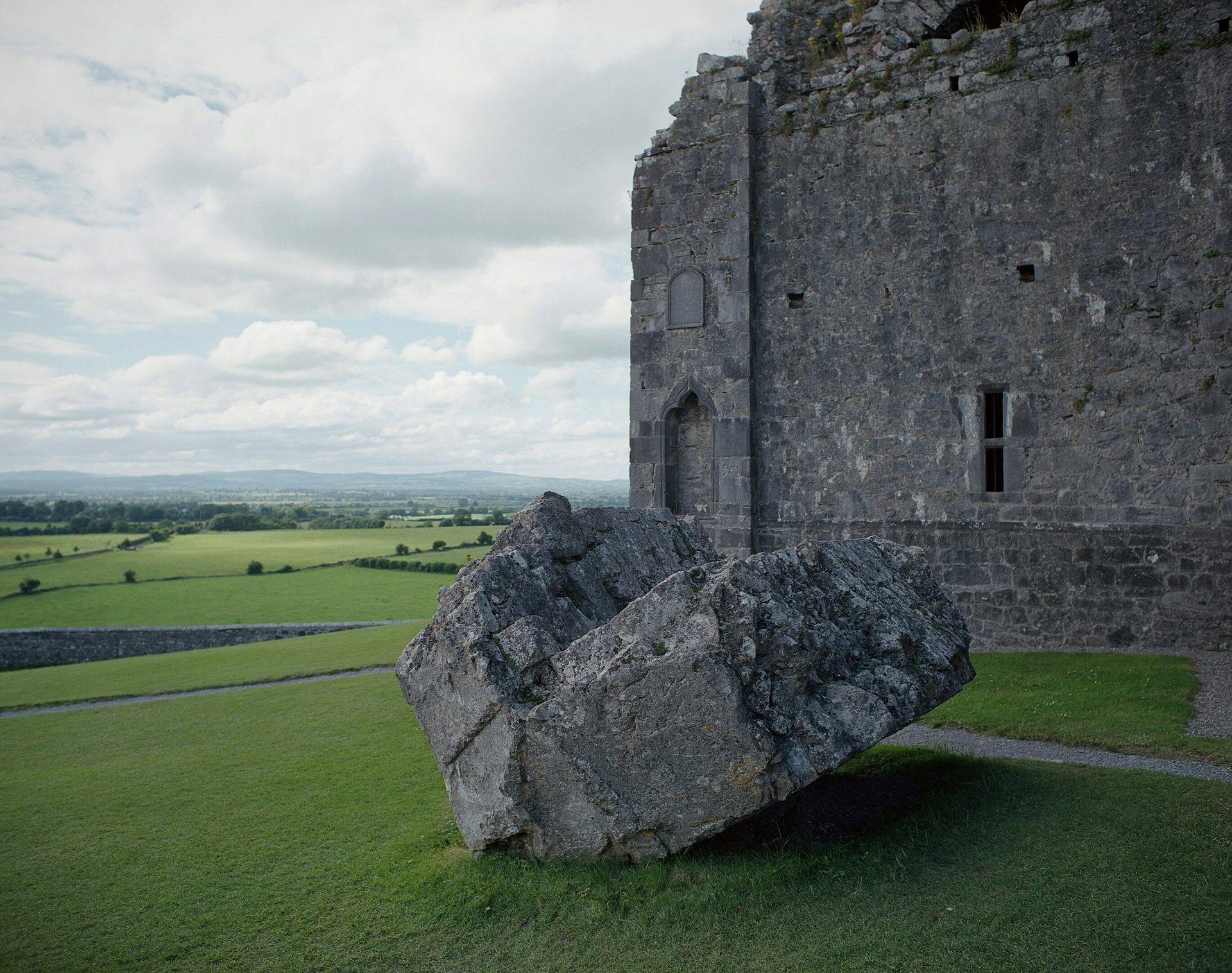 A castle with a huge chunk of its ramparts broken off and sitting on the grass beneath.