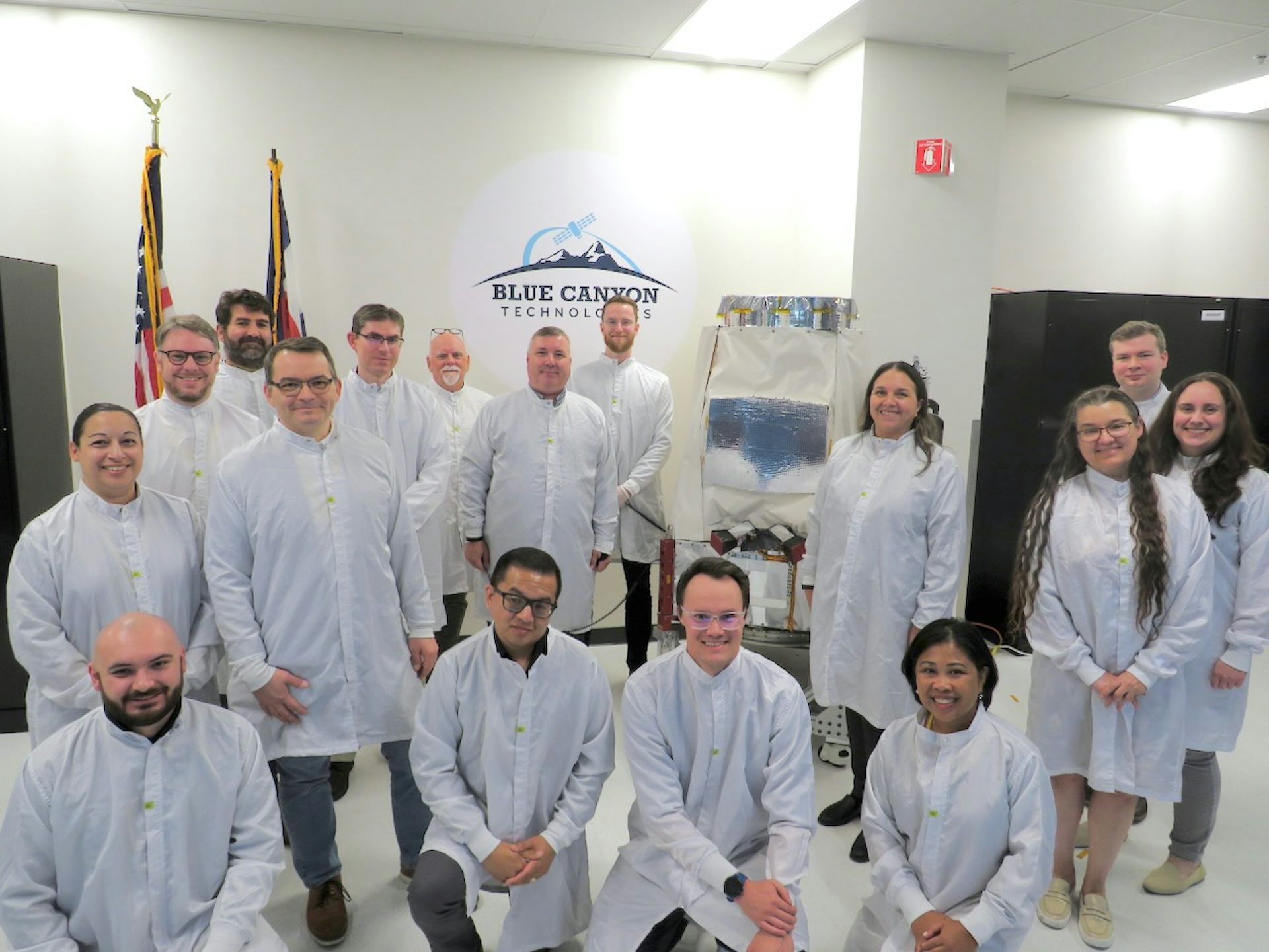 A group of people wearing lab coats, standing next to a satellite.