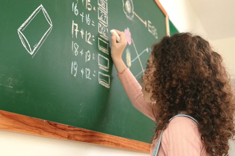 Une élève résout des opérations de maths sur un tableau.