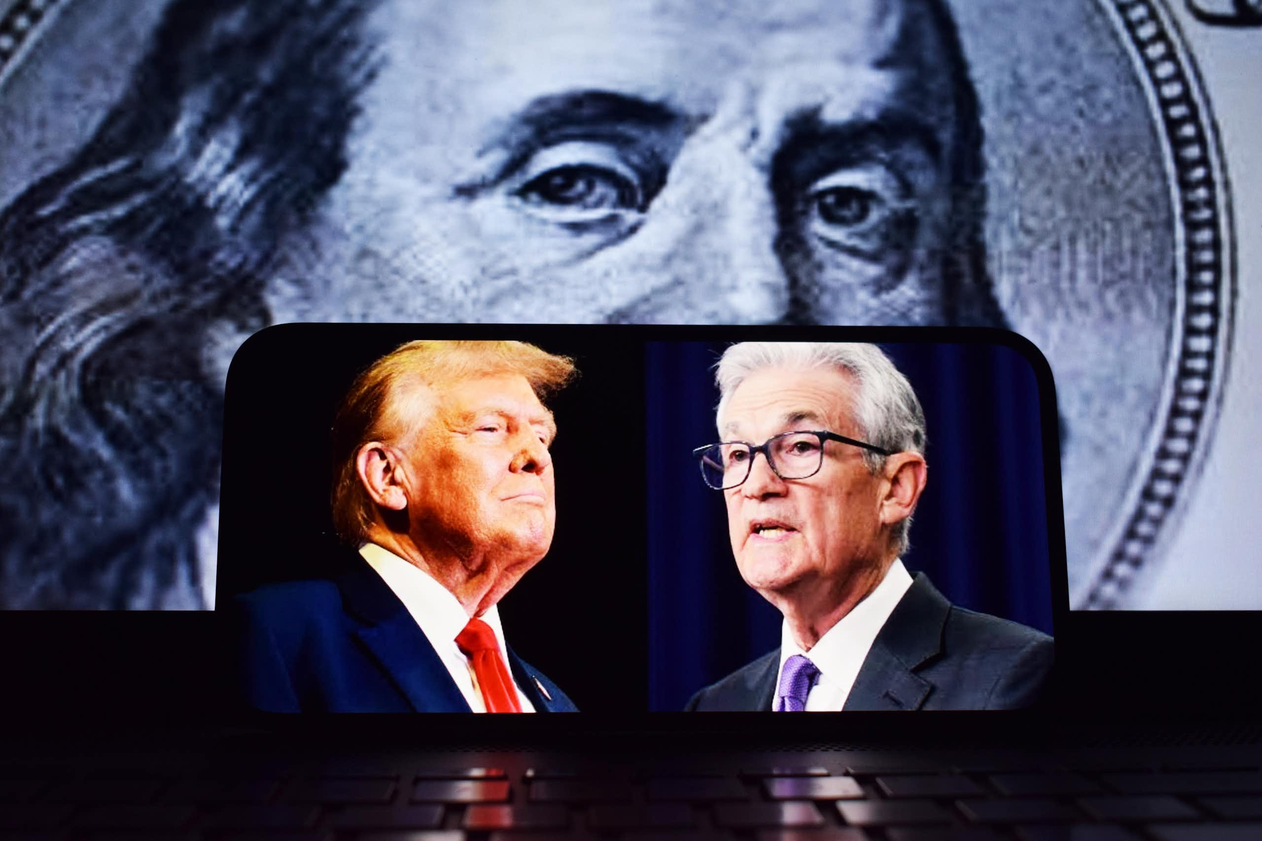 Donald Trump et Jerome Powell sur un portable avec un billet de dollar en fond.