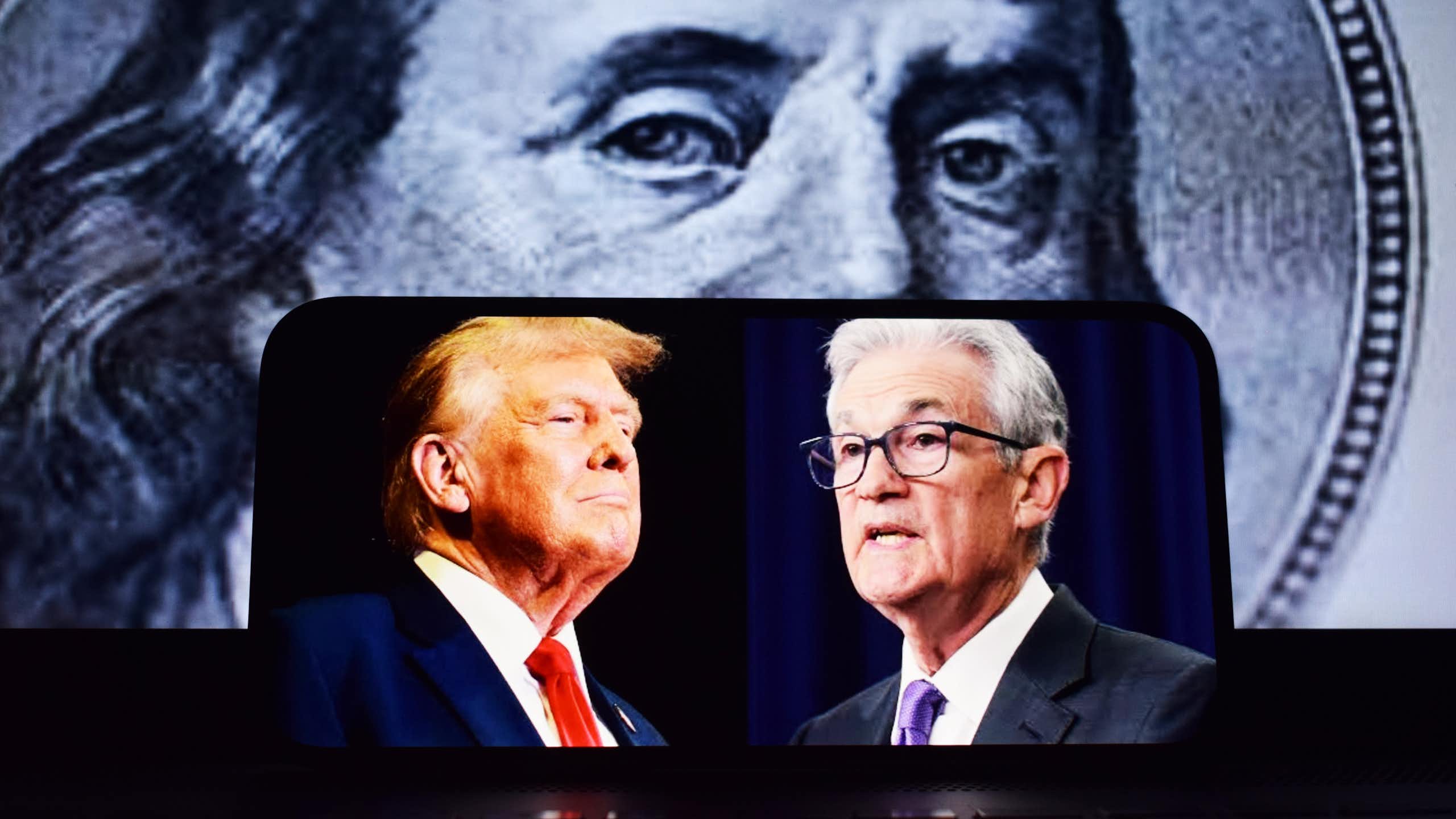 Donald Trump et Jerome Powell sur un portable avec un billet de dollar en fond.