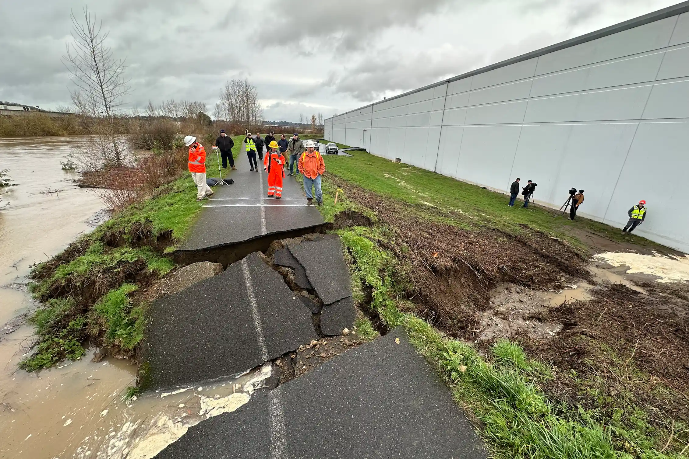 A paved bicycling path atop a levee is broken and slabs of asphalt pavement are tilted into a breach where water poured through.