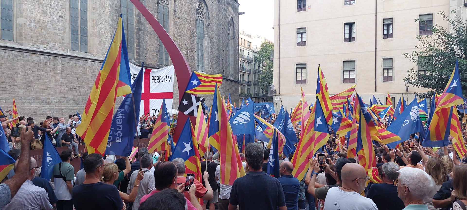 A group of people with Aliança Catalana flags gathered in a square
