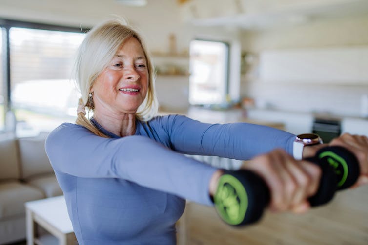 A woman in a blue top using small hand weights