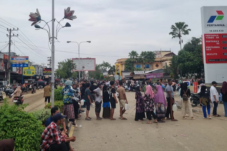 People stand holding jerrycans in long lines at a fuel station
