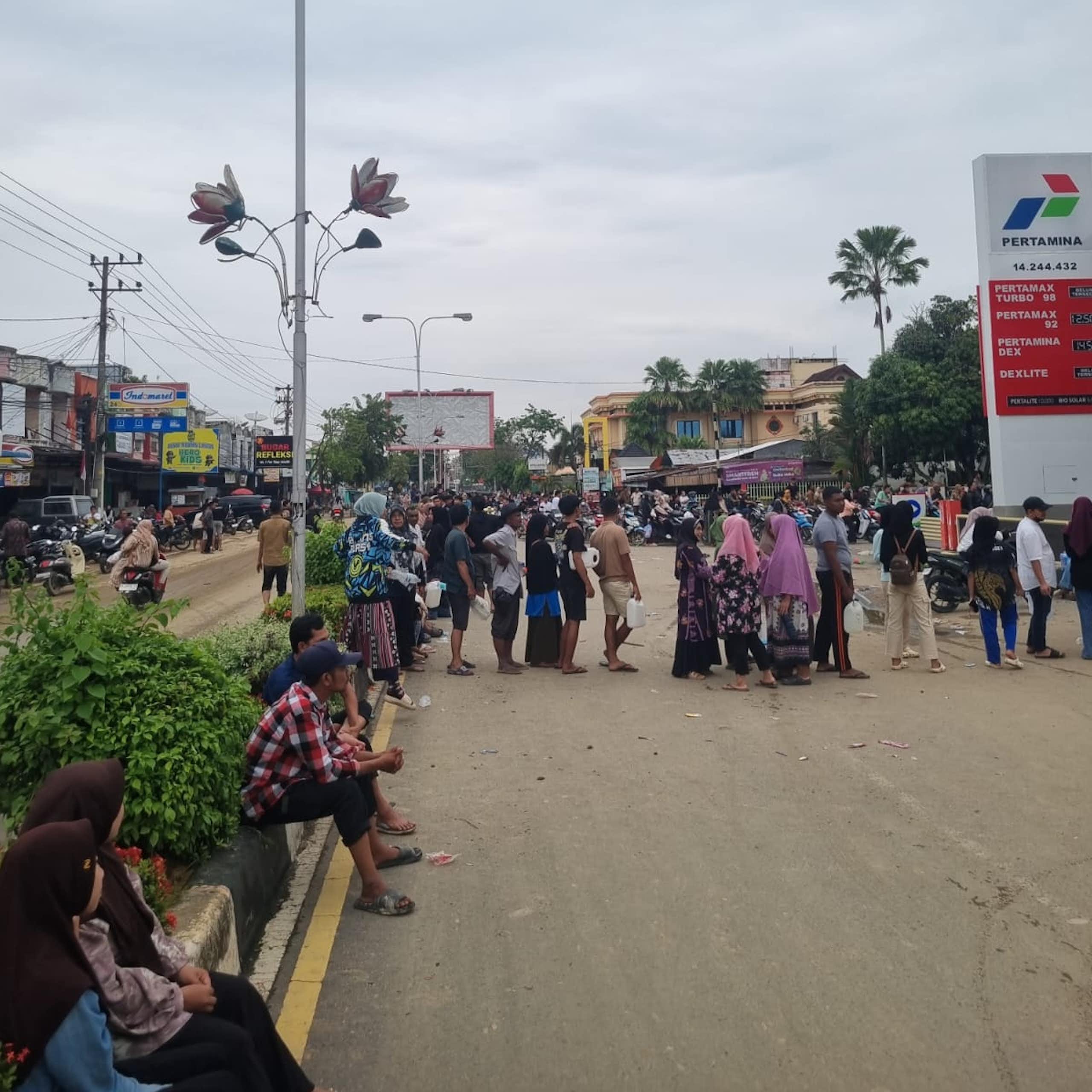 People stand holding jerrycans in long lines at a fuel station