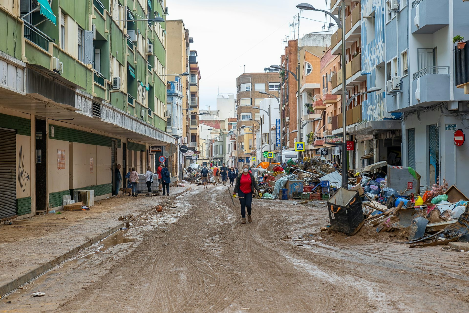 Un carrer ple de fang i deixalles amb una dona i persones de fons.