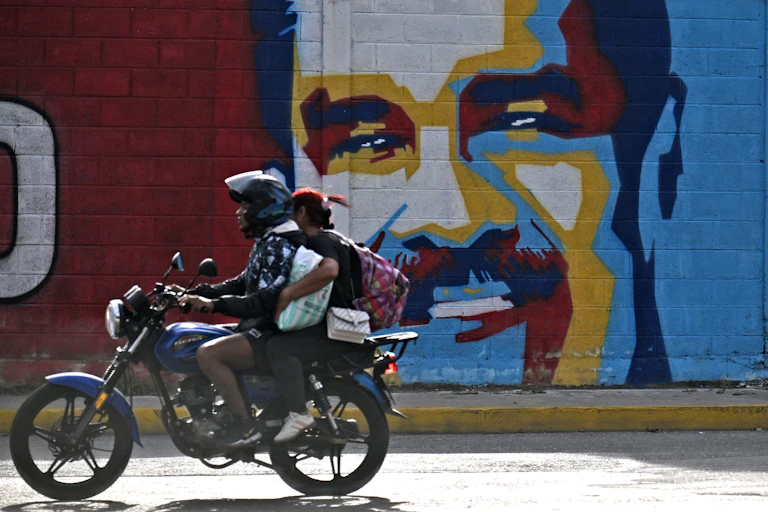 A man on a motorcycle drives past a mural of a man's face.