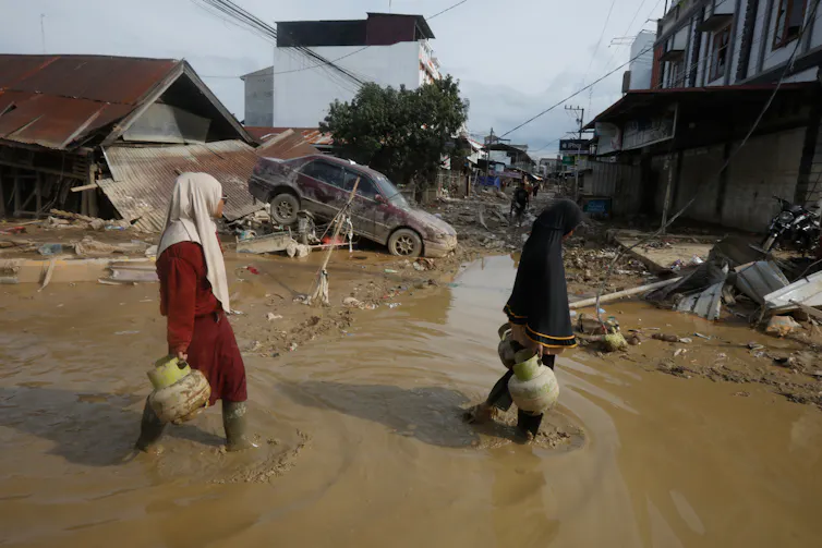 women walk through floodwaters near damaged buildings