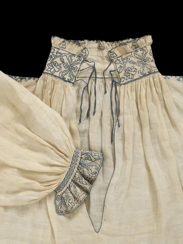 A linen shirt with blue embroidery around the collar and cuffs.