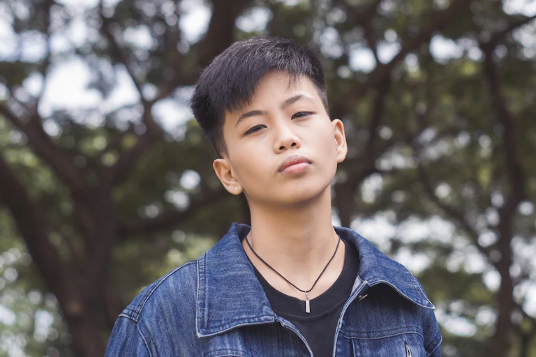 Young non-binary person stands in front of trees.