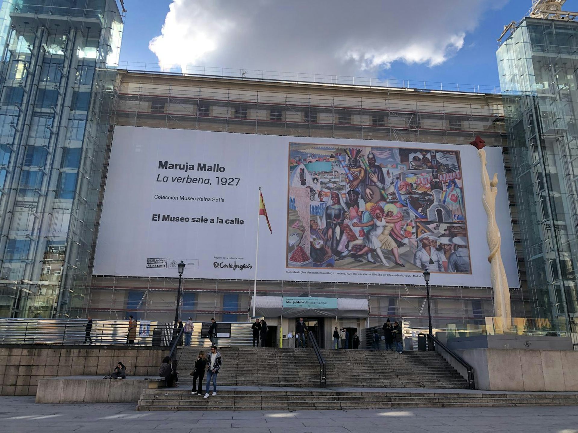 Fachada de un museo con una lona que muestra un cuadro colorista de Maruja Mallo que retrata una verbena.