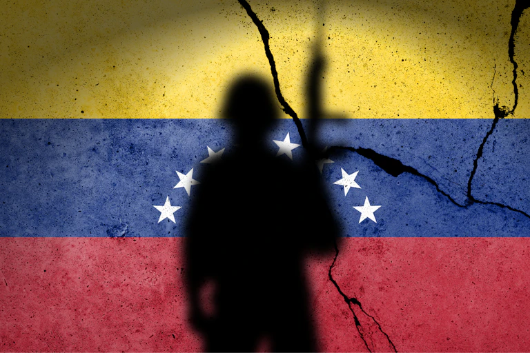 Una sombra de soldado con una bandera venezolana agrietada al fondo.