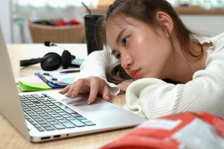 Une jeune femme qui travaille sur son ordinateur en s'ennuyant.