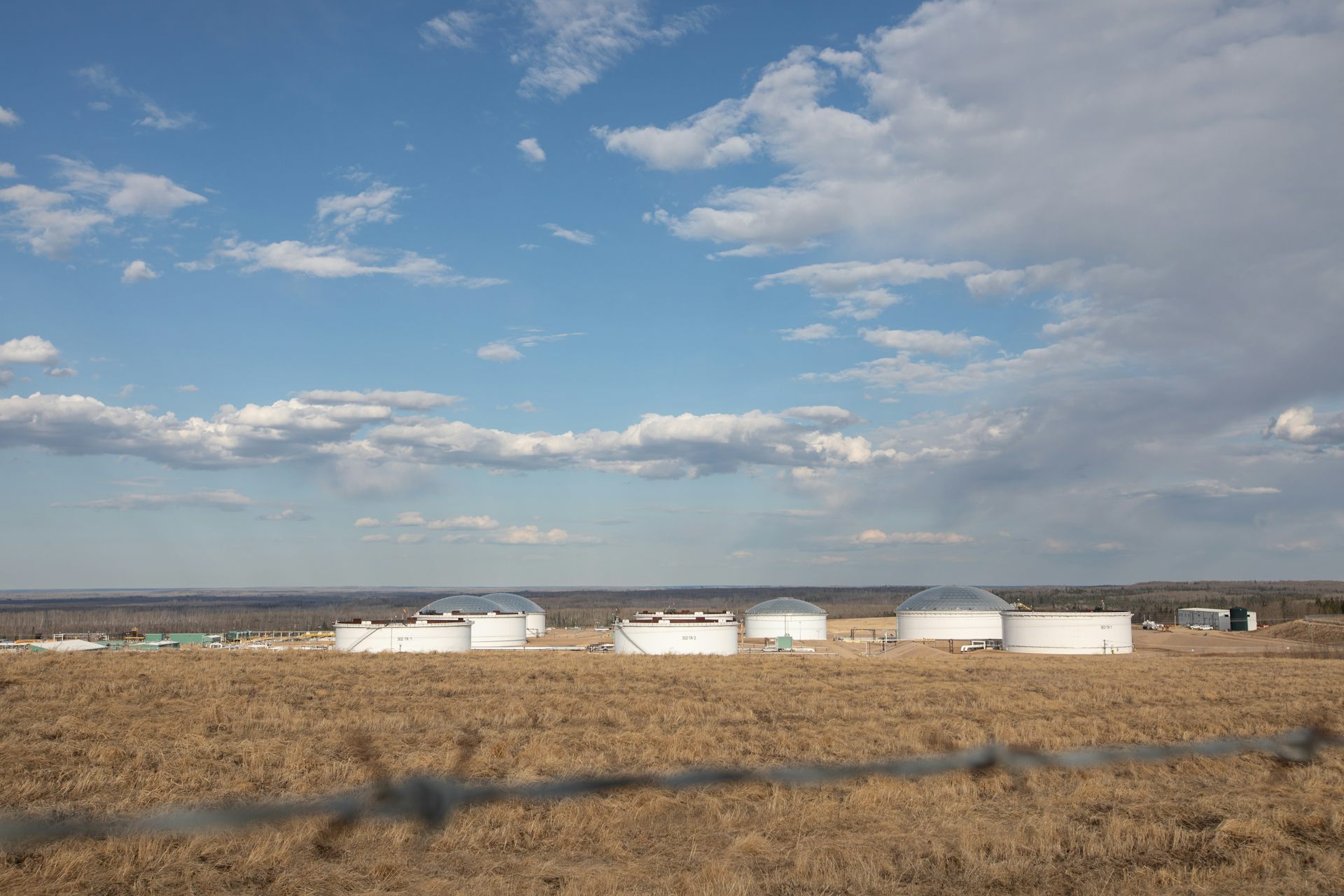Varios edificios blancos bajos en un campo de pradera bajo un cielo azul fotografiados desde la distancia.