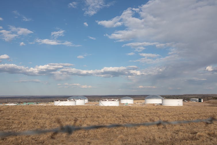 Varios edificios blancos bajos en un campo de pradera bajo un cielo azul fotografiados desde la distancia.