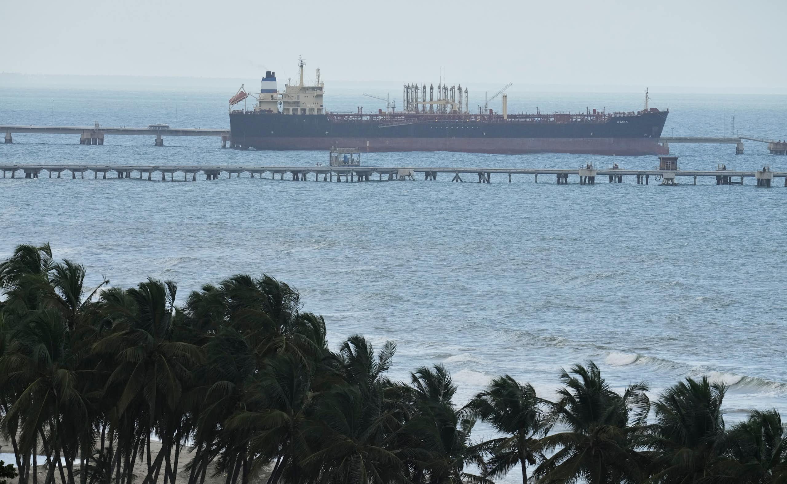 Palm trees in the foreground as an oil tanker sits docked at a por