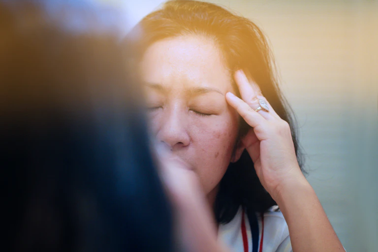 Reflection of stressed middle-aged woman with eyes closed and hand to head