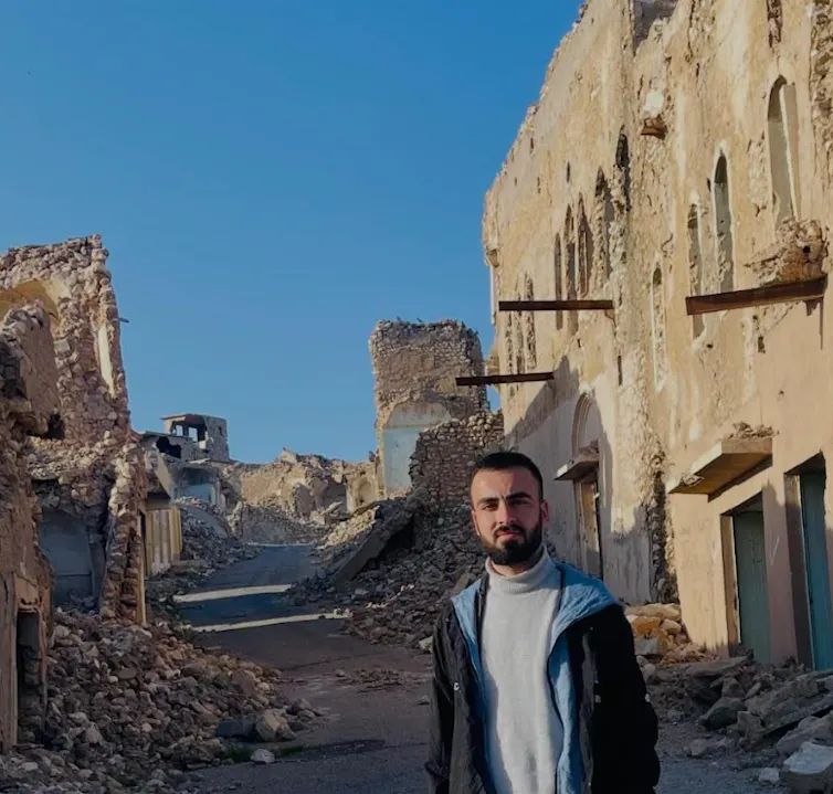 Man stands among ruins.