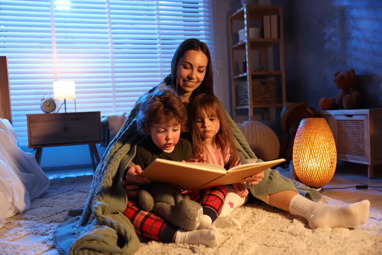 Mother reading with children under blanket