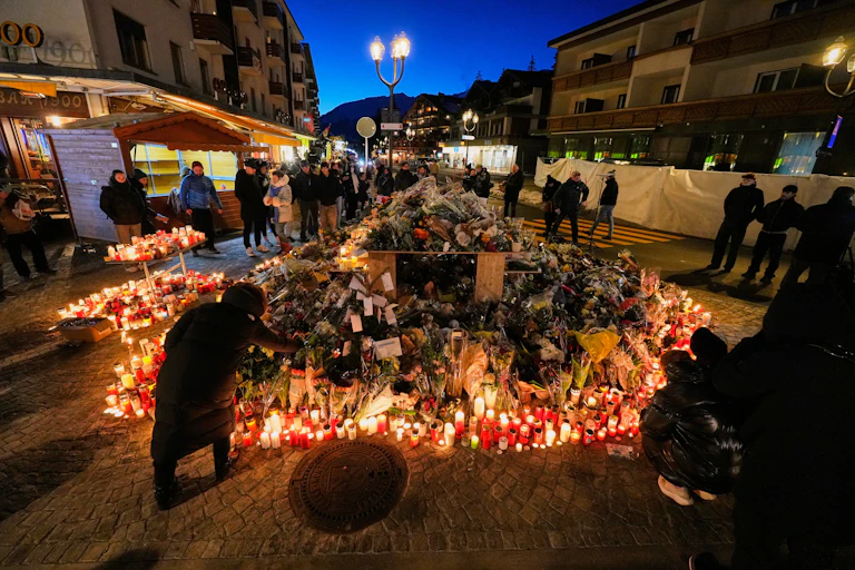 a large display of many candles outdoors, people stand around, some light candles