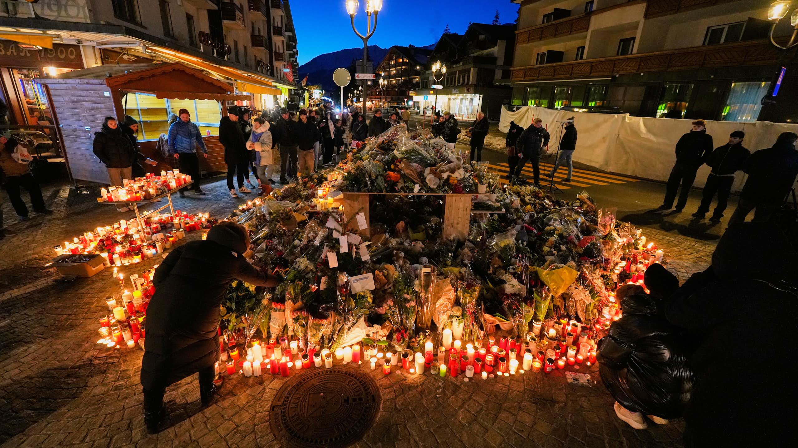 a large display of many candles outdoors, people stand around, some light candles