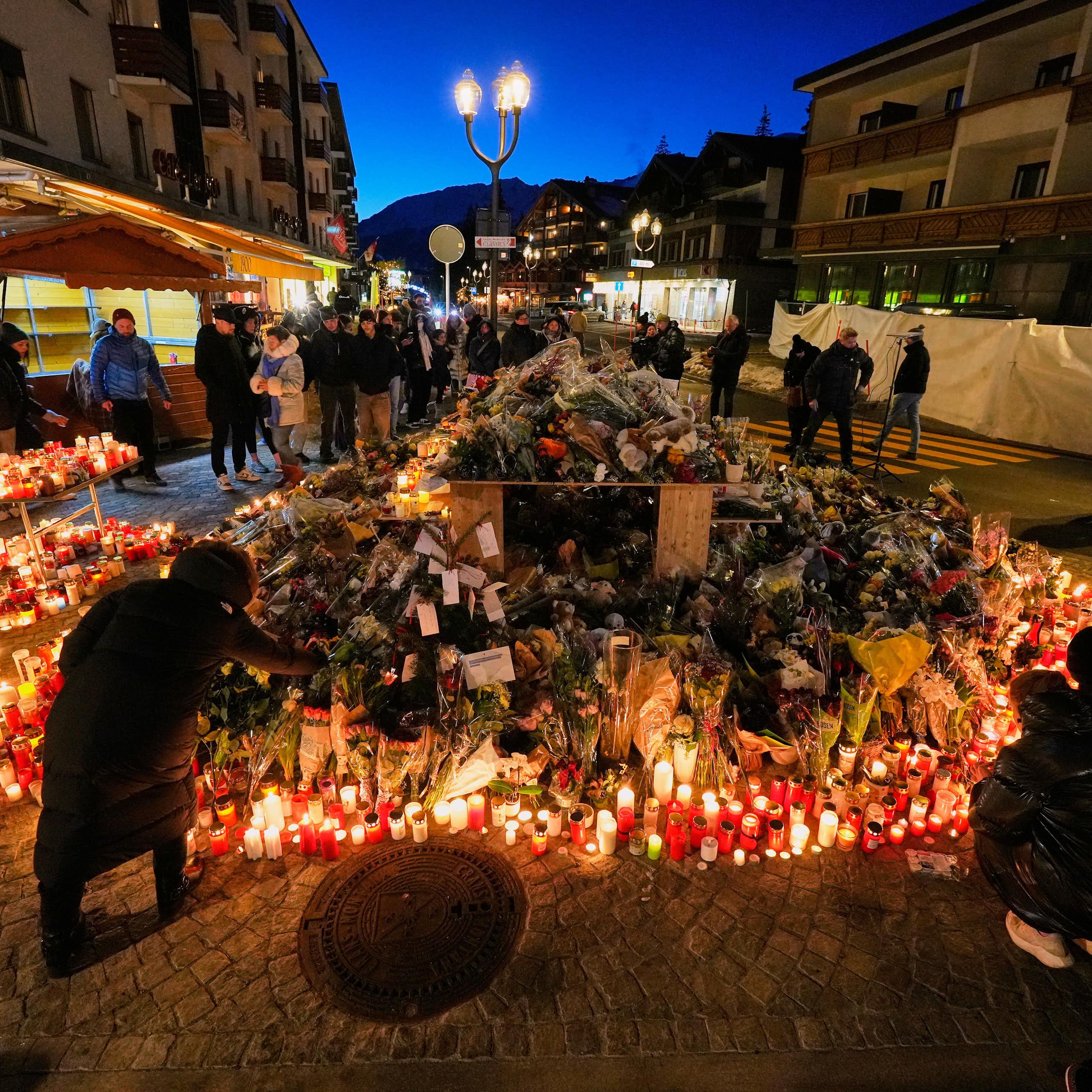 a large display of many candles outdoors, people stand around, some light candles