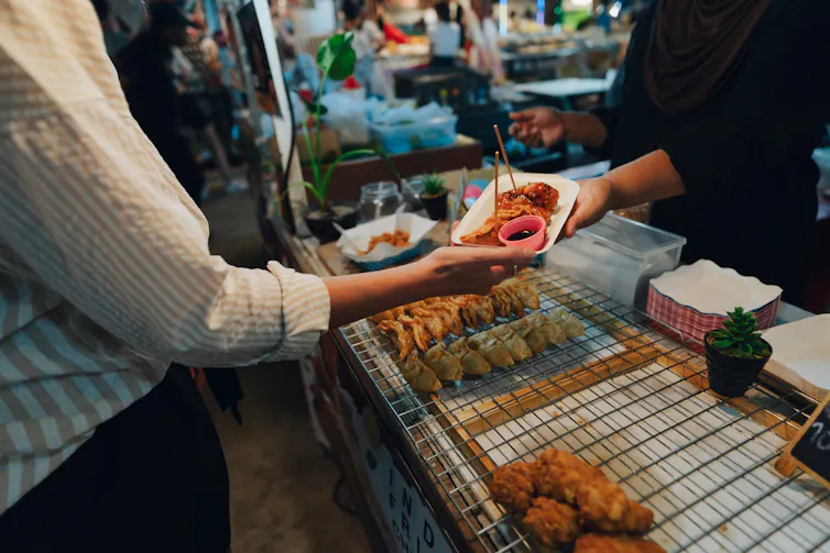 Dans un kiosque de nourriture, une personne tend à une autre une assiette en carton remplie de nourriture