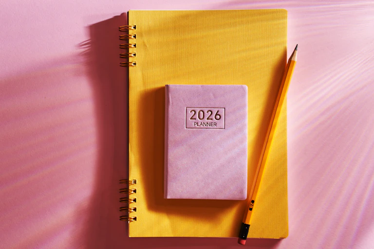 A 2026 planner and pencil are seen against a pink background